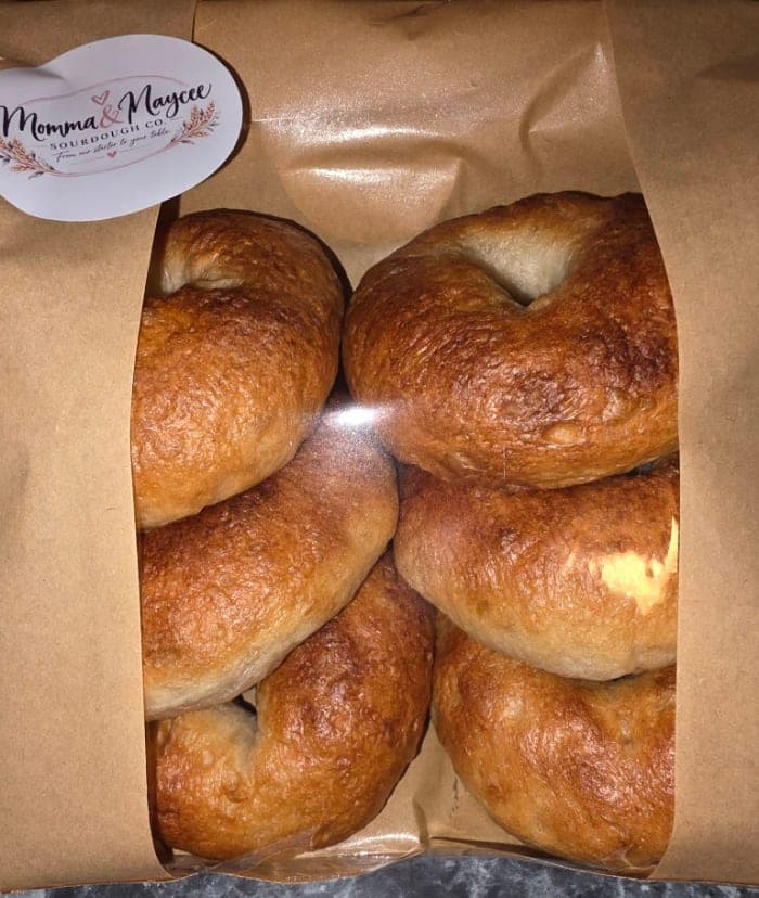 Six golden plain sourdough bagels packed in a kraft bag with a Momma & Maycee Sourdough Co. sticker